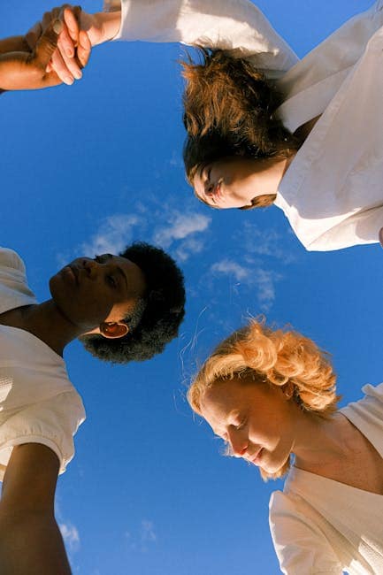 Three women holding hands under a clear blue sky, symbolizing unity and friendship.